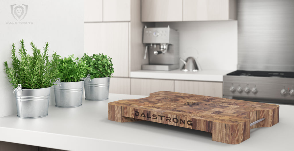 Wooden cutting board in a clean white kitchen next to three small potted plants on the counter
