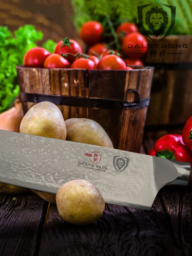 proformapeakmarketing Shogun Series Kiritsuke knife on a wooden table surrounded with potatoes, and buckets of tomatoes, pepper, and other vegetables.